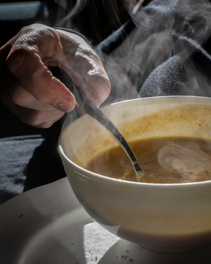 En hånd holder om en ske i en varm skål suppe