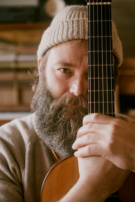 Musiker Thomas Alstrup holder en guitar op foran venstre side af ansigtet, mens han kigger ind i kameraet