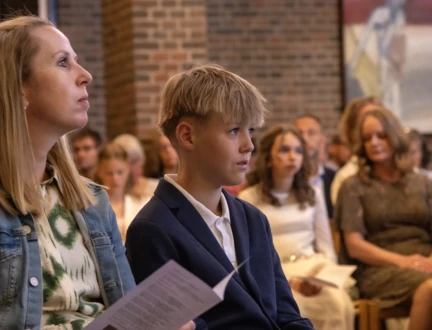 To konfirmander sidder på deres særlige pladser i kirken under en konfirmation.